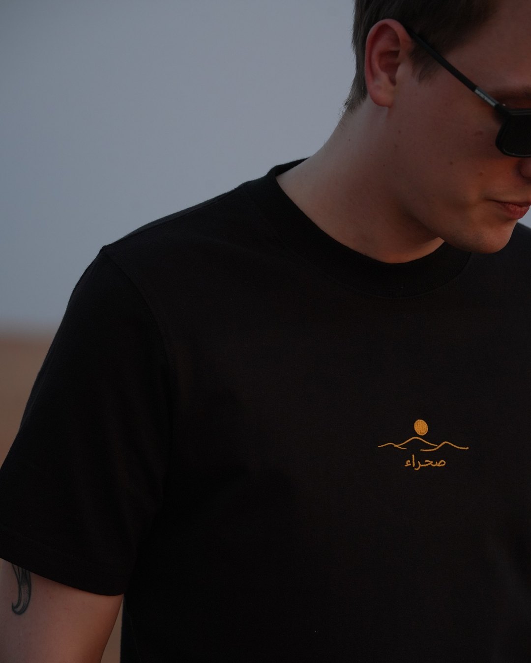 The Al Quaa Galaxy tee, chest close — the embroidered mark on black cotton