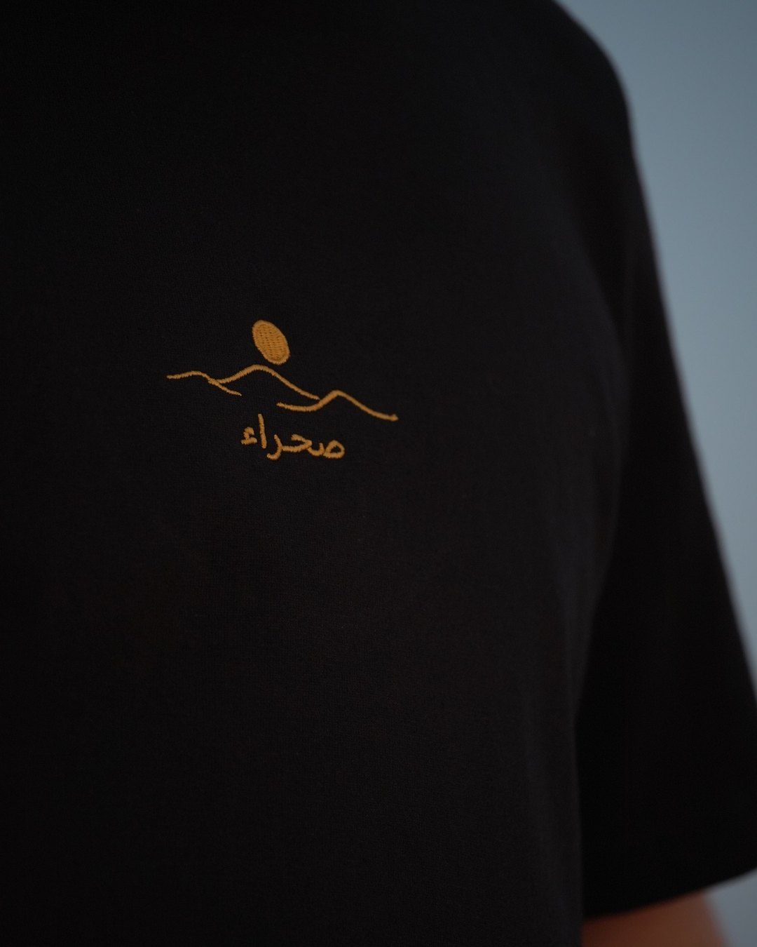 The Al Quaa Galaxy tee, the embroidered صحراء mark in gold, close