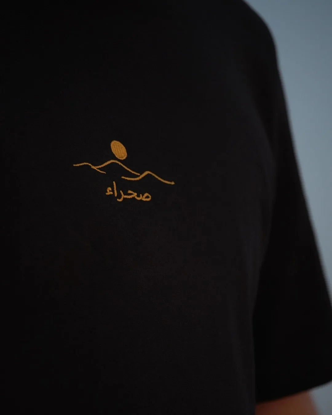 The Al Quaa Galaxy tee, the embroidered صحراء mark in gold, close