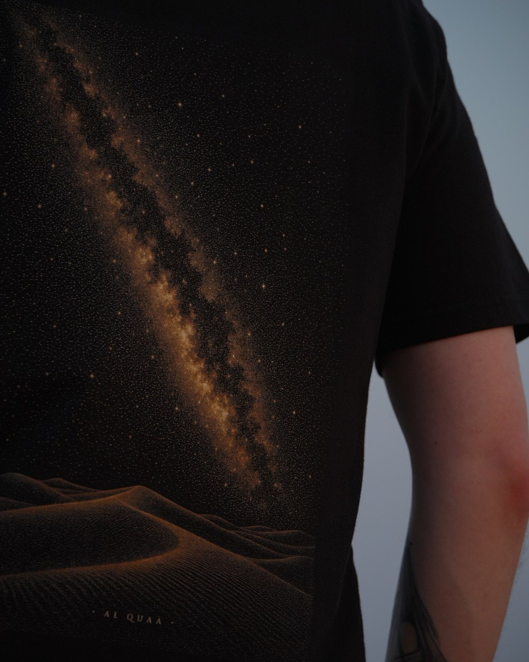 The Al Quaa Galaxy tee, the printed band at an angle — the grain of the stars across the shoulder