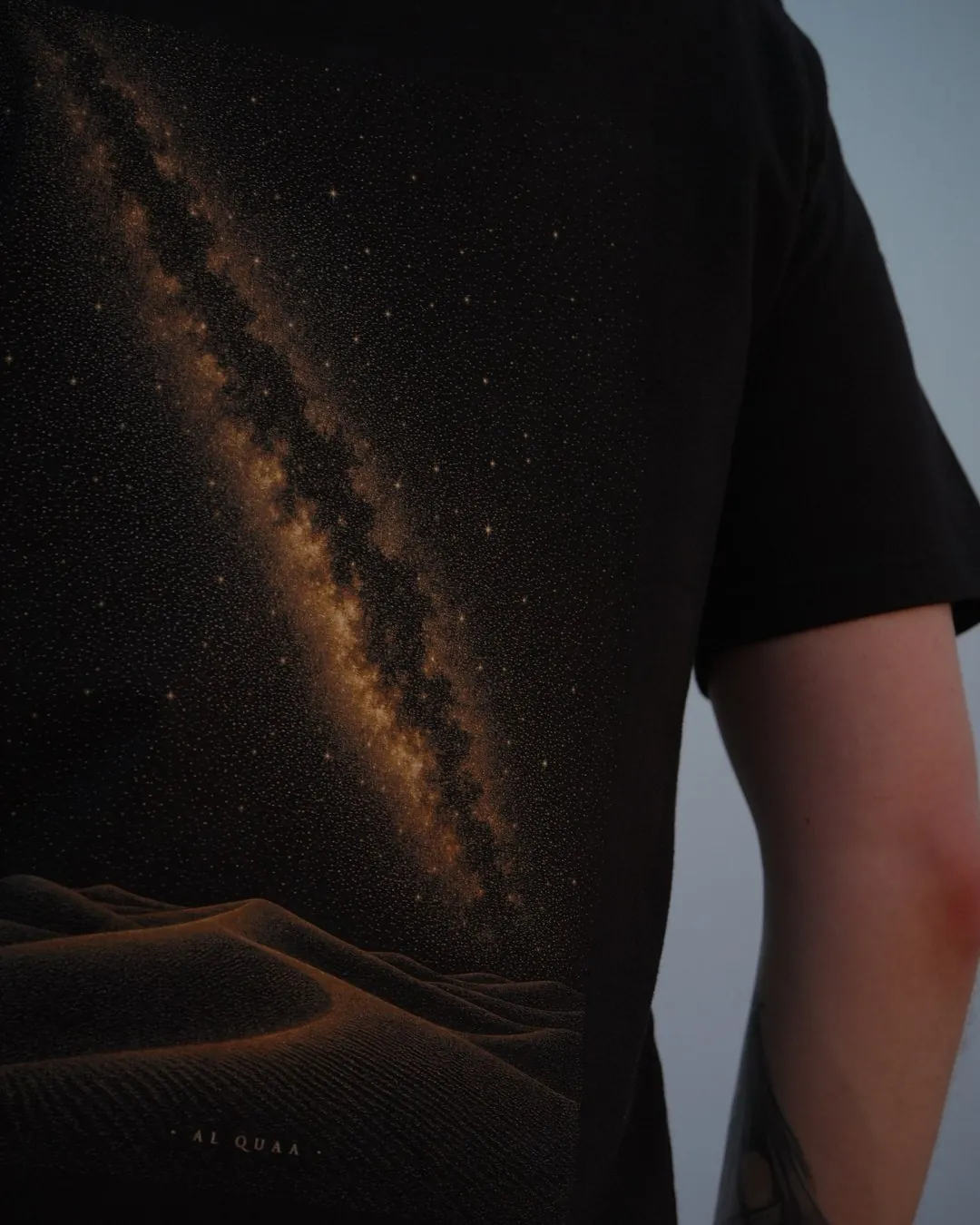 The Al Quaa Galaxy tee, the printed band at an angle — the grain of the stars across the shoulder