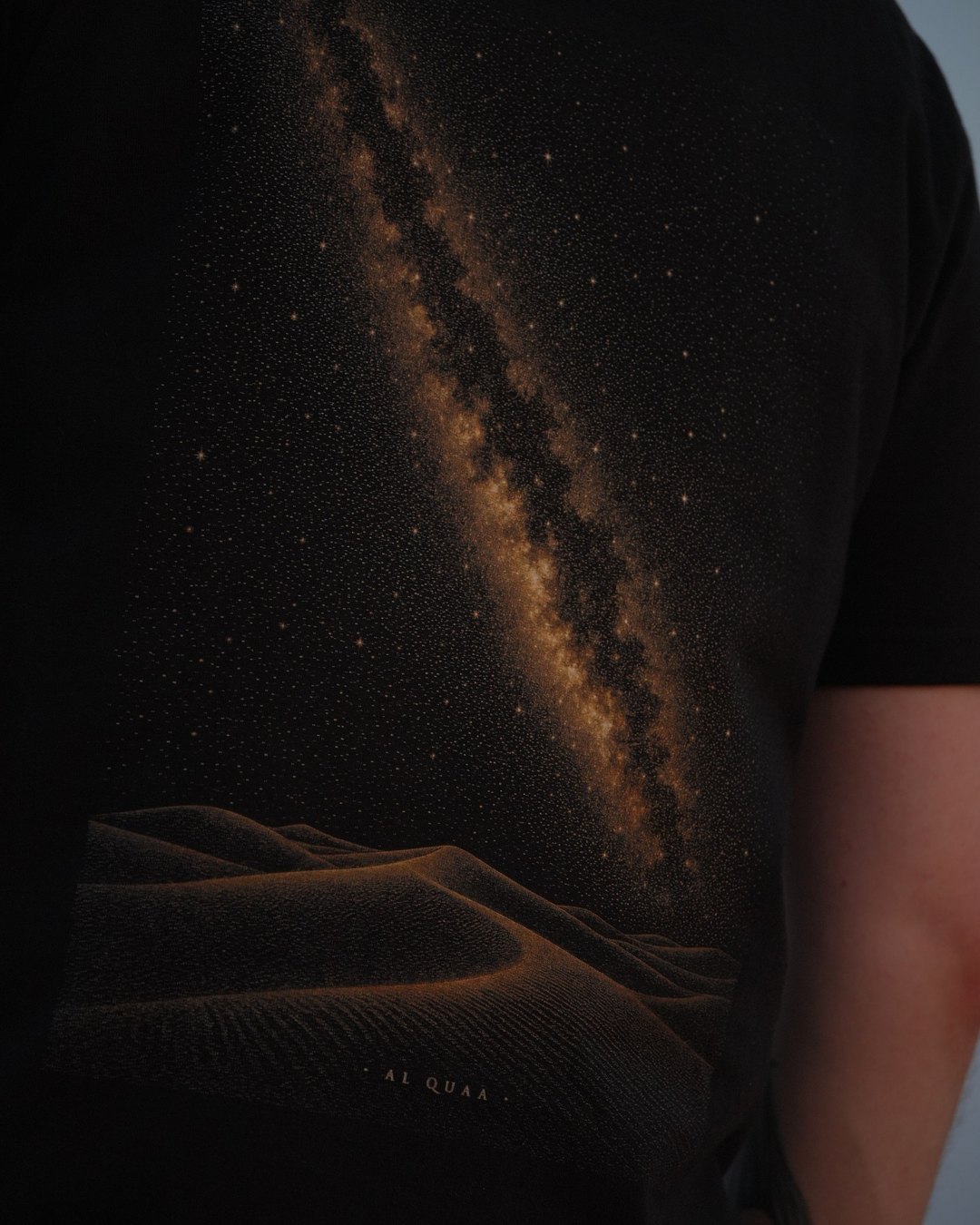 The Al Quaa Galaxy tee, back print close — the gold stipple of the Milky Way over the dune line
