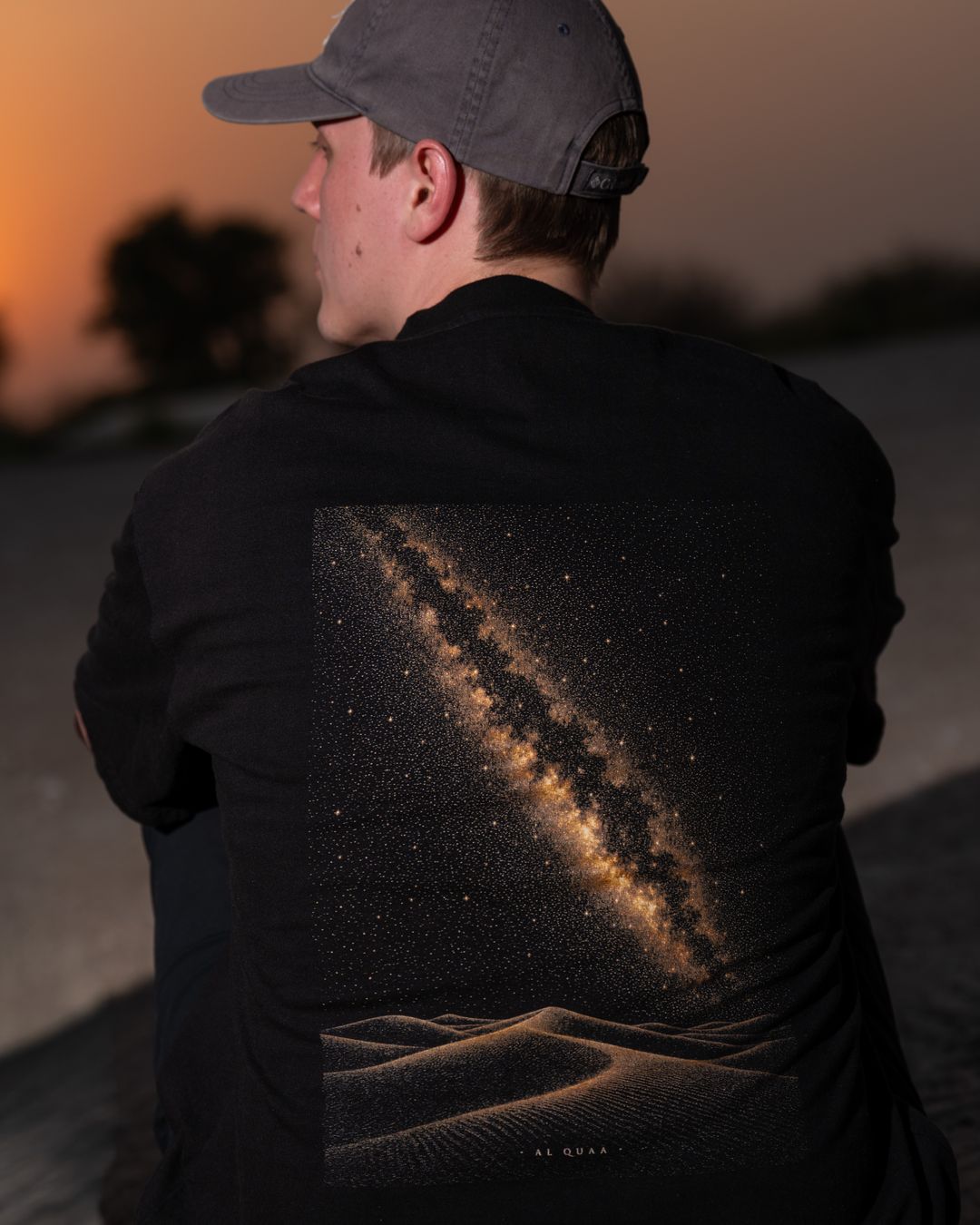 The Al Quaa Galaxy tee from behind at golden hour — the Milky Way print across the back, close. Male model wears M in the Oversized fit.