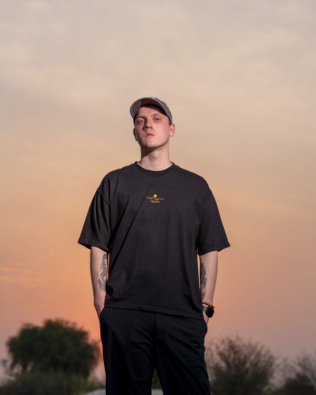 The Al Quaa Galaxy tee worn front-on against the evening sky — the gold embroidered mark on the chest. Male model wears M in the Oversized fit.