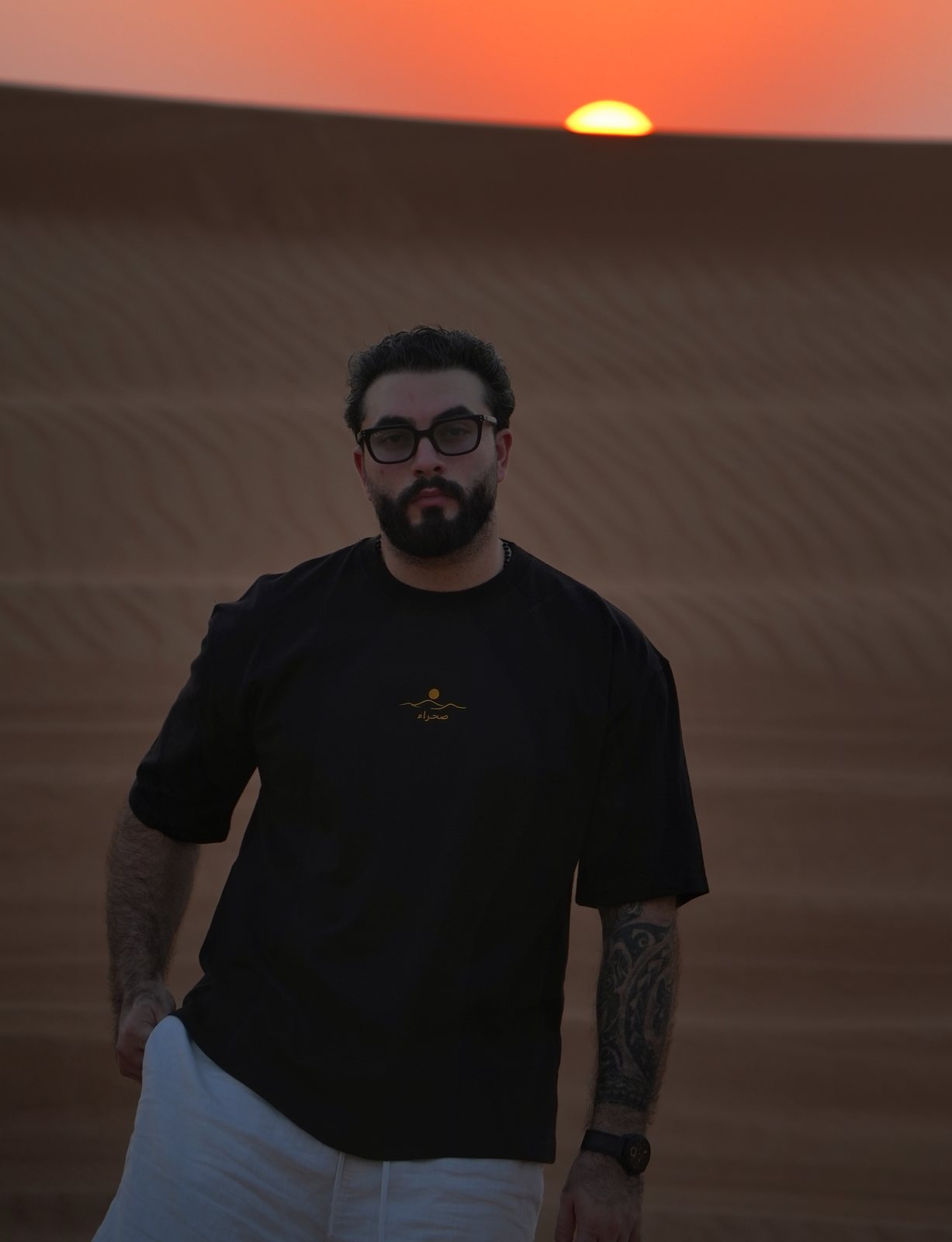 The Al Quaa Galaxy tee worn facing the last light, embroidered chest mark catching the gold