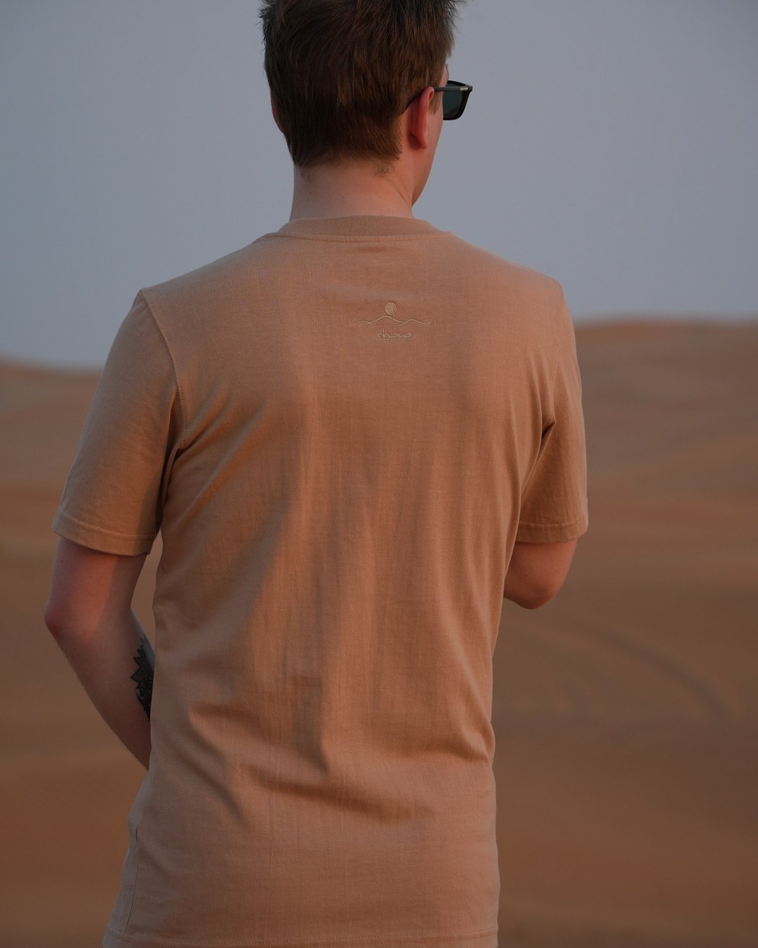 The Empty Quarter tee from behind in the dunes — plain across the back