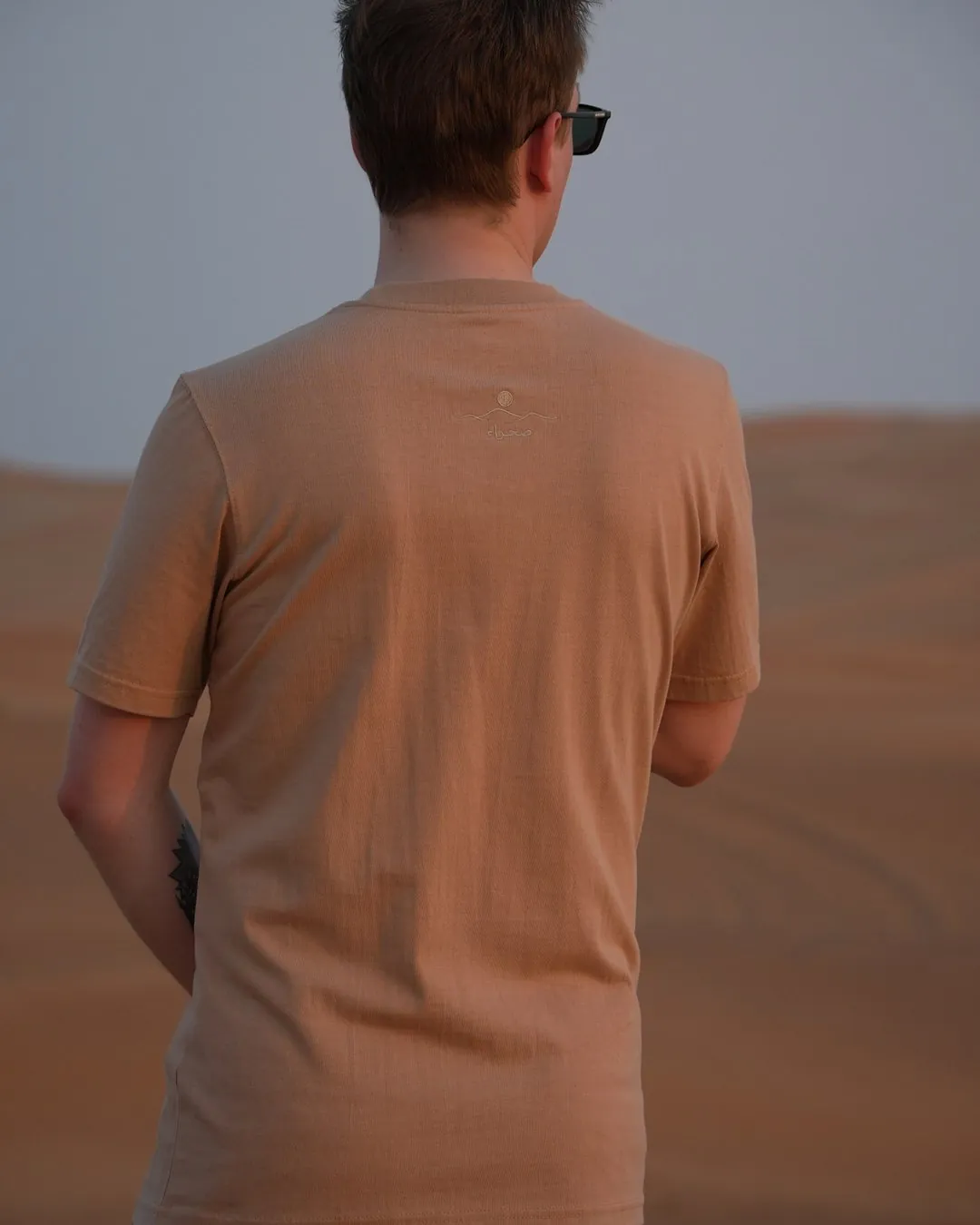 The Empty Quarter tee from behind in the dunes — plain across the back