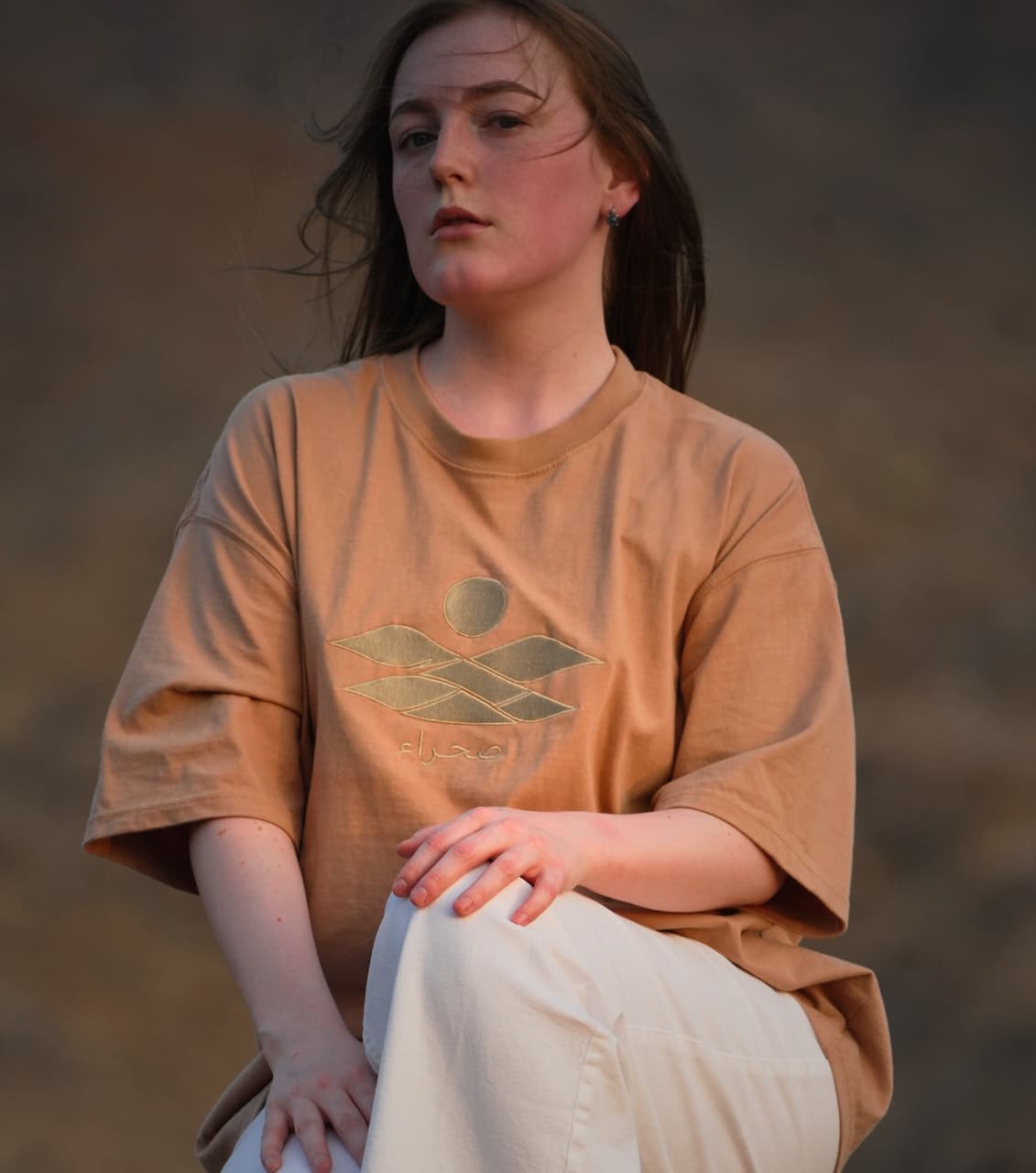 The Empty Quarter tee worn seated on the rocks in the mountains. Female model wears M in the Oversized fit.