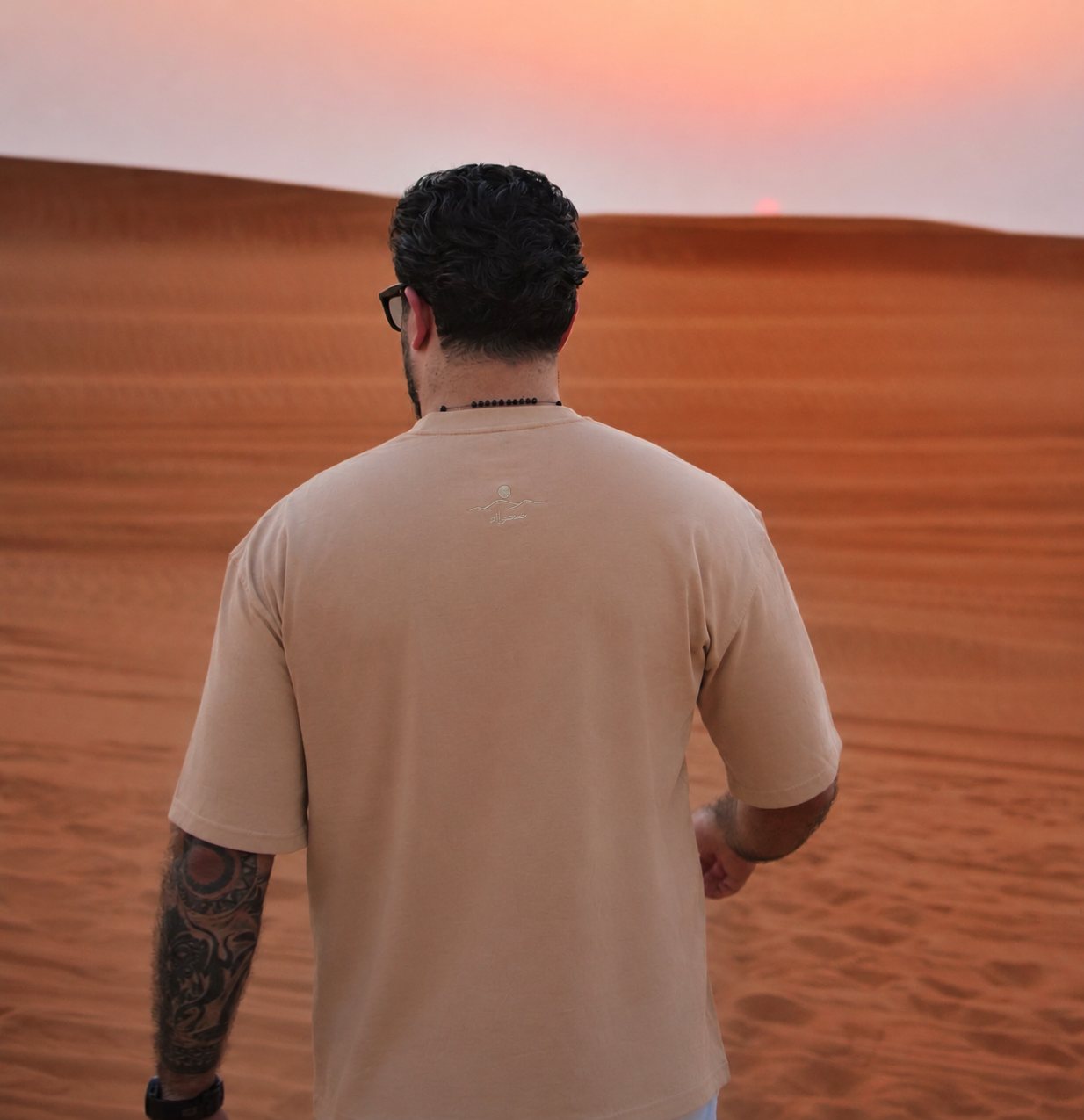 The back of the Empty Quarter tee at sunset, back-neck embroidery visible over the dunes