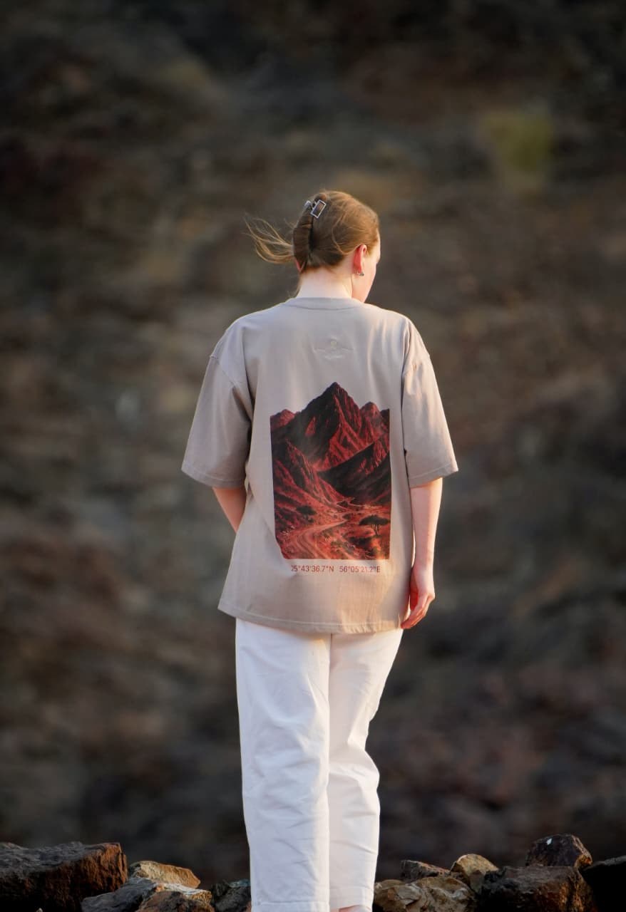 The back of the Hajar Mountains tee in the mountains — the red-rock print across the back. Female model wears M in the Oversized fit.