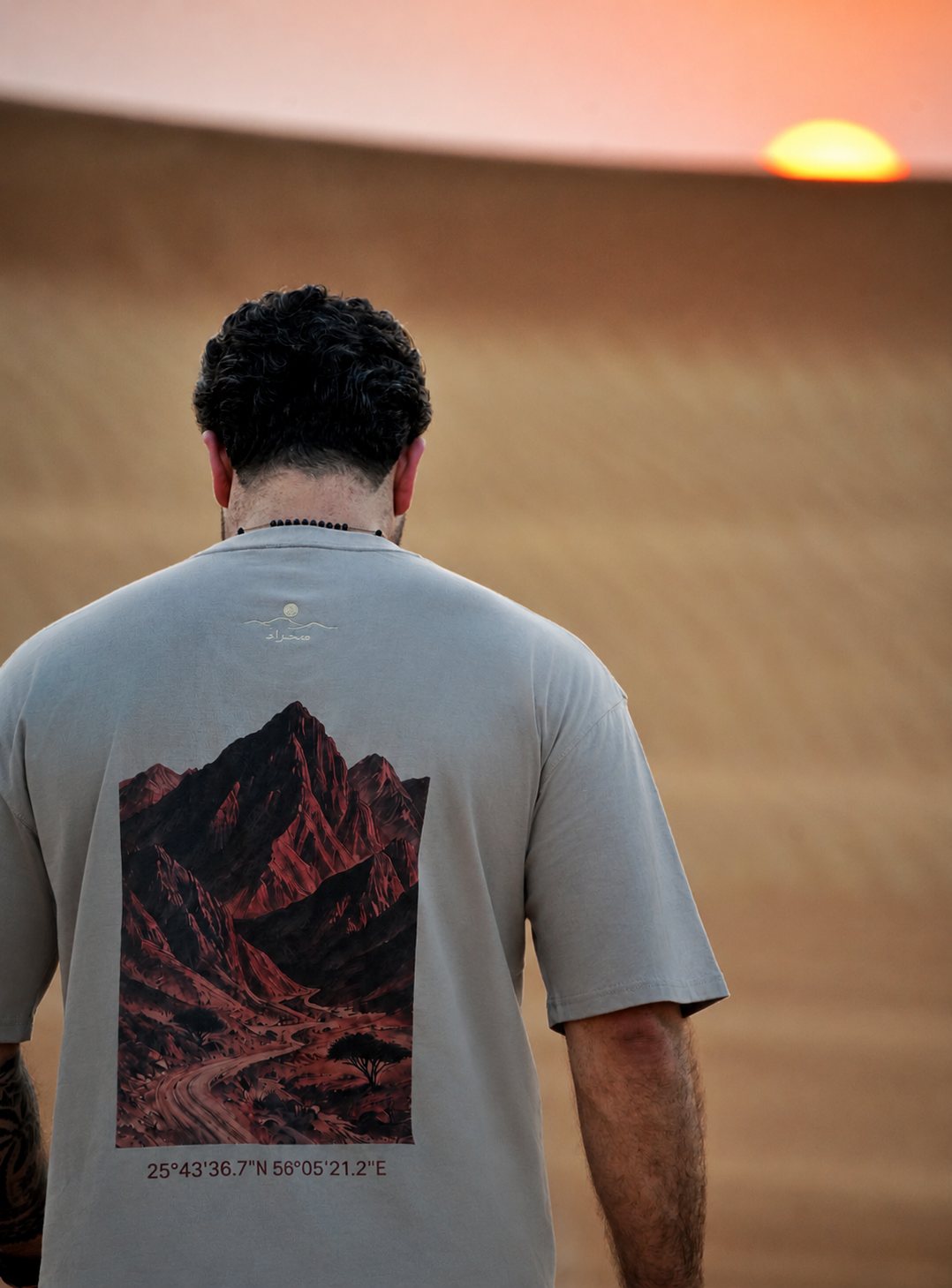 The Hajar Mountains tee worn at sunset — the mountain print and Wadi Naqab coordinates across the back