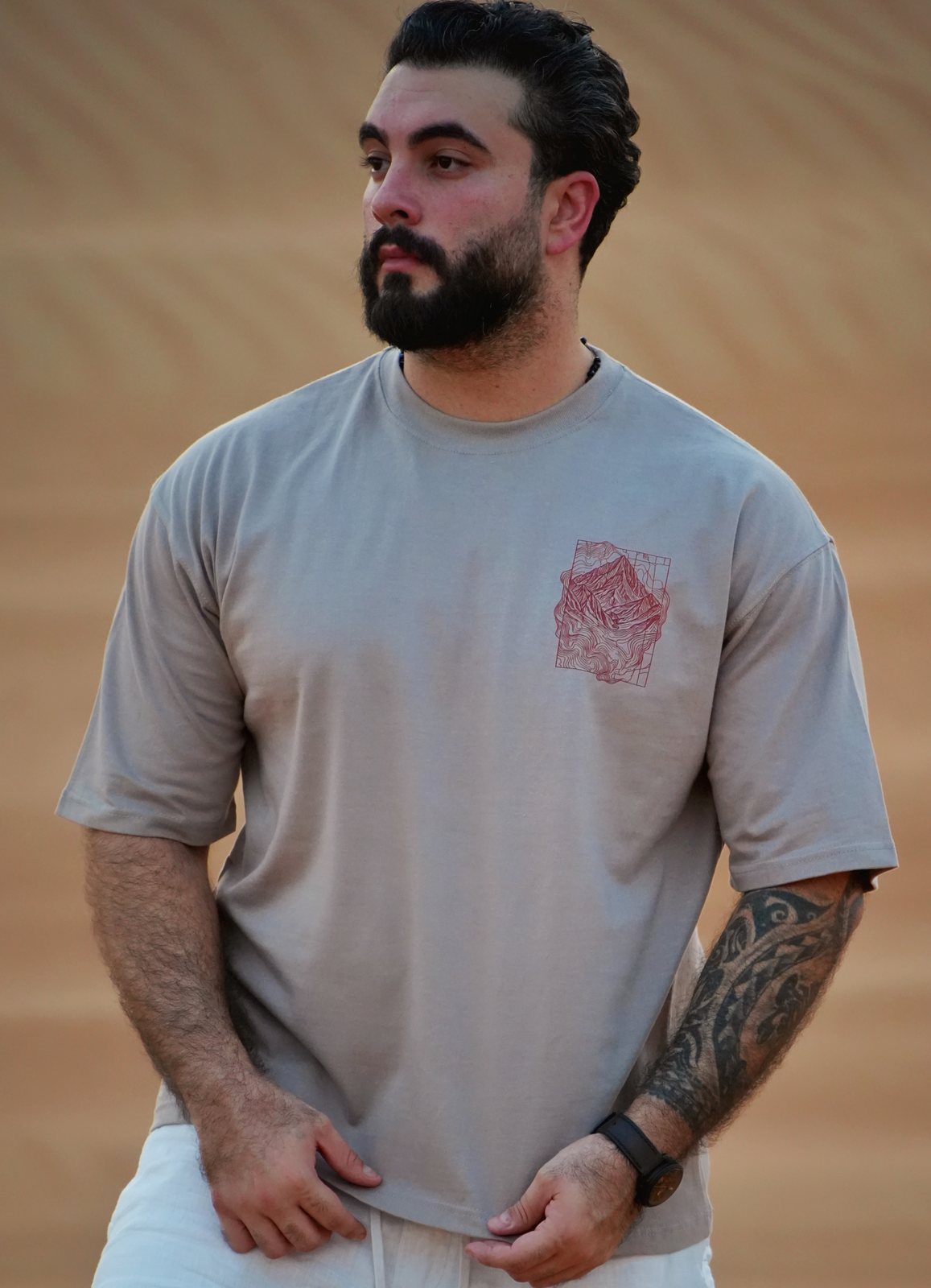 The Hajar Mountains tee worn in the dunes — the contour-line mountain print on the chest