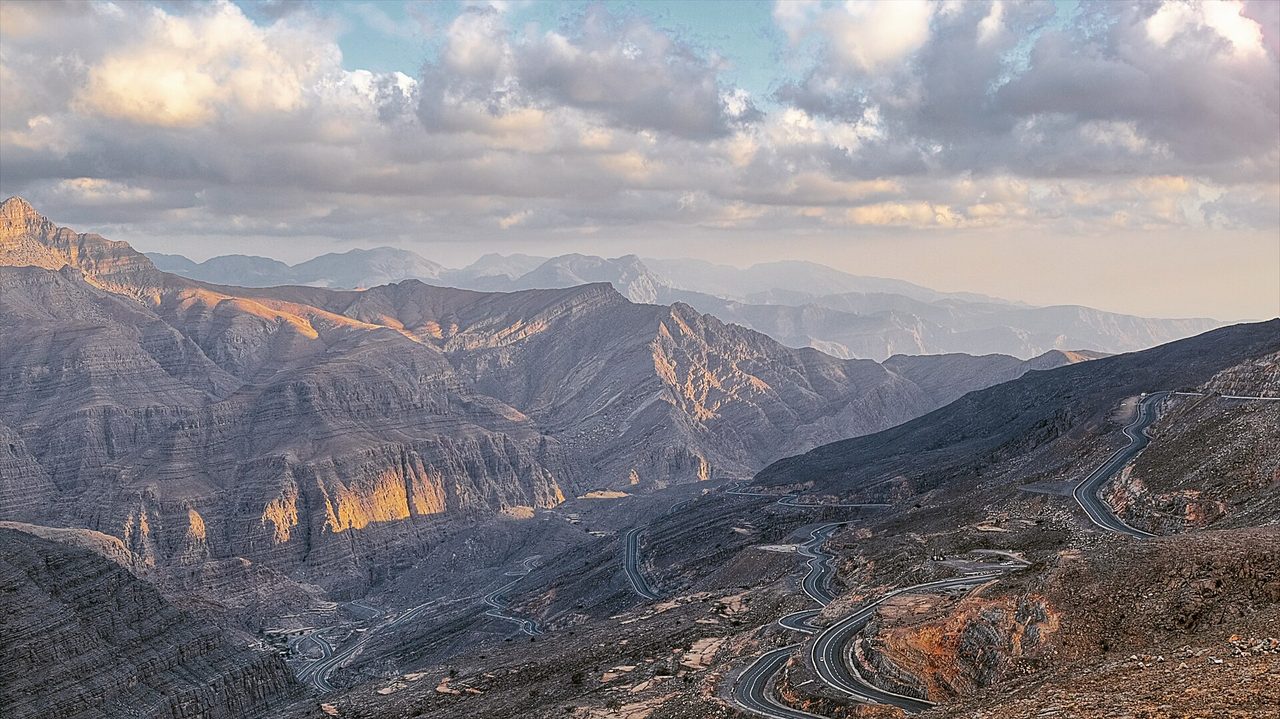 Sunlit rock ridges of the Hajar Mountains with the winding Jebel Jais road below, seen from near the top of the mountain