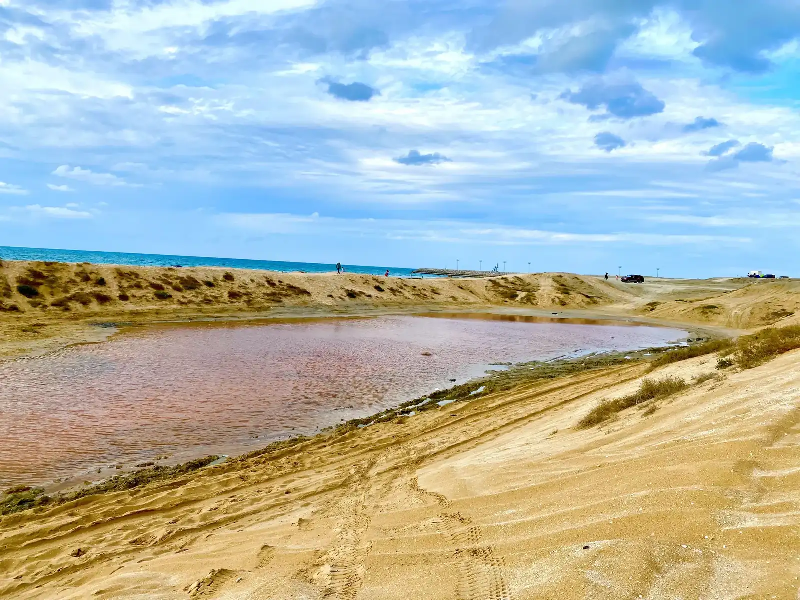 A pink lagoon behind the dunes on Saraya Island, with the sea beyond