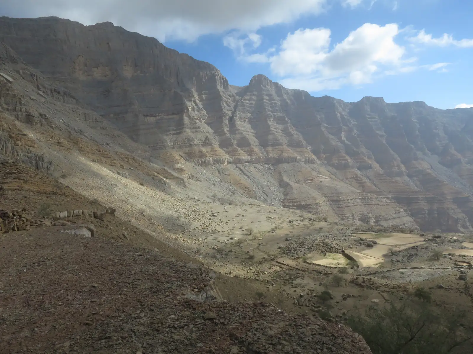 A layered limestone wall of the Hajar Mountains near Jebel Jais, with old terraced fields below