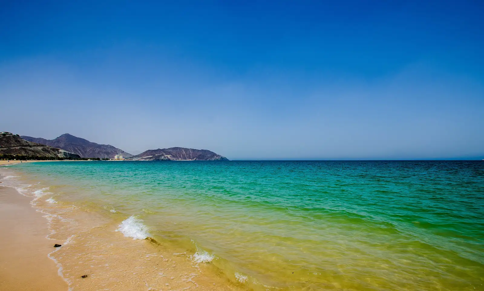 Clear green water and sand at Khor Fakkan Beach, with the Hajar Mountains at the end of the bay