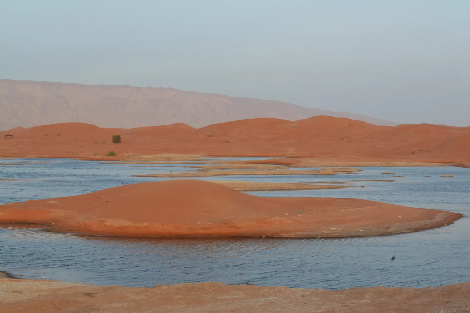 Zakher Lake's water and a red sand island against the Hajar Mountains, Al Ain